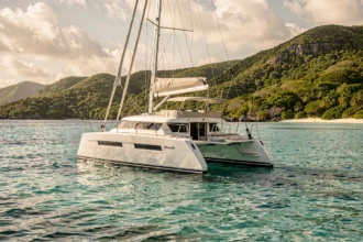 Catamaran blanc ancré dans un lagon turquoise des Grenadines avec collines verdoyantes en arrière-plan