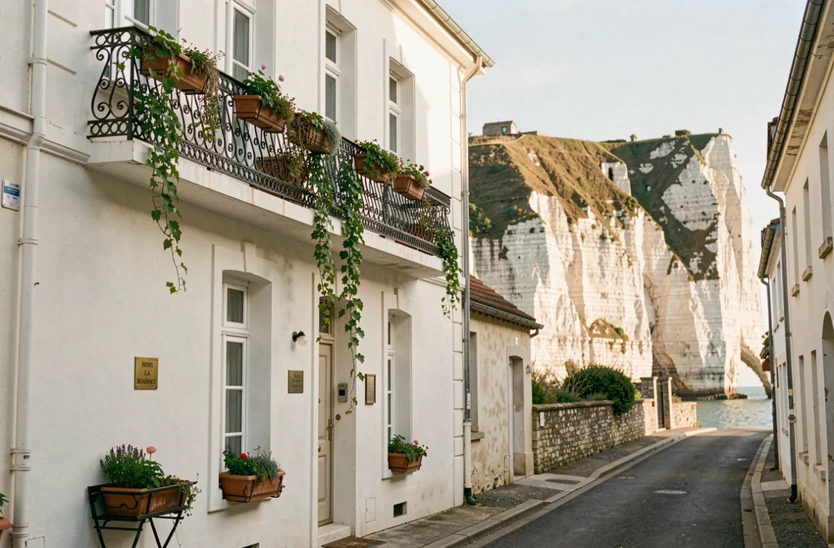 Façade de l'Hôtel La Résidence à Étretat avec ses balcons en fer forgé et les célèbres falaises d'albâtre visibles dans la ruelle derrière l'établissement